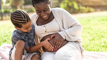 Happy African family expecting other baby - Afro Mother and son touching pregnant belly doing heart shape with hands - Parents love and maternity lifestyle concept photo