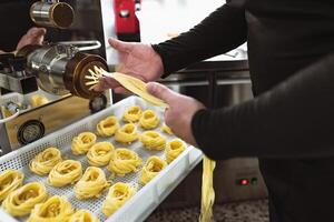 Close up male hands preparing fresh fettucine using machine inside pasta factory photo