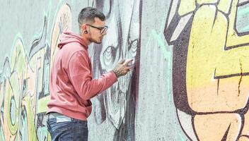 Street graffiti artist painting with a color spray can a dark monster skull graffiti on the wall in the city- Urban, lifestyle street art concept - Main focus on his hand photo