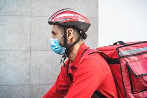 jinete hombre entregando comida a clientes con eléctrico bicicleta mientras vistiendo cara máscara durante corona virus brote - eco rápido entrega comida concepto foto