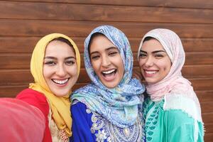 Happy Muslim girls taking selfie outdoor - Arabian young friends portrait making self photo for social media network - Religion culture and youth millennial lifestyle concept - Wooden background