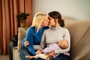 Happy lesbian couple having tender moments with their small baby at home - Family and materhood concept photo