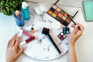 Top view young woman doing makeup at home - Closeup female hands applying make up - Cosmetic and skincare advertising concept photo