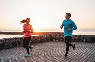 ajuste Pareja corriendo en puesta de sol hora siguiente el playa - deportivo joven personas haciendo rutina de ejercicio sesión al aire libre - saludable, juventud y deporte actividad estilo de vida concepto foto