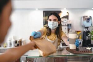 bar propietario trabajando solamente con tomar lejos pedidos durante corona virus brote - joven mujer trabajador vistiendo cara quirúrgico máscara dando eliminar comida a clientes - cuidado de la salud y comida bebida concepto foto