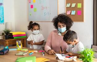 Female teacher with children drawing in preschool classroom while wearing face protective mask during corona virus pandemic - Healthcare and education concept photo