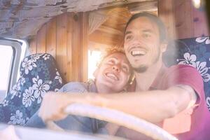 Happy smiling couple inside a vintage minivan - Travel people excited driving for a road trip with a van camper - Vacation, love, relationship lifestyle concept photo