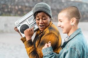 contento multirracial mujer teniendo divertido bailando mientras escuchando a música con Clásico boombox estéreo foto