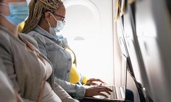 Senior woman using laptop during airplane trip while wearing face mask photo