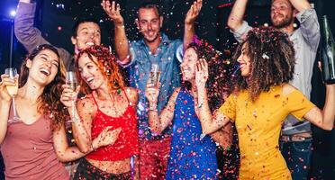 Happy friends doing party dancing and drinking champagne at nightclub - Millennial young people having fun celebrating together and throwing confetti - Entertainment, youth lifestyle holidays concept photo