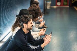 joven personas utilizando móvil teléfono inteligente mientras sentado en subterraneo estación esperando tren - juventud milenario fanático a nuevo tecnología concepto foto