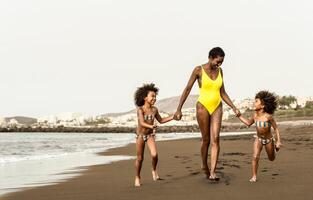Happy Afro family having fun running on the beach during summer time - Parents vacations and travel lifestyle concept photo