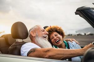 Happy senior couple having fun driving on new convertible car - Mature people enjoying time together during road trip tour vacation - Elderly lifestyle and travel culture transportation concept photo