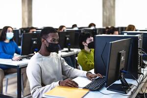 joven multirracial estudiantes tomando un examen en alto colegio mientras vistiendo cara máscara durante corona virus pandemia - educación y tecnología concepto foto