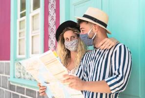 Young couple wearing face mask and holding travel map - Travelers people enjoying first trip after corona virus outbreak - Restart tourism and love relationship vacation lifestyle concept photo