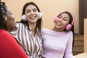 Happy multiracial friends having fun listening music with wireless headphones on house patio - Young people lifestyle concept photo