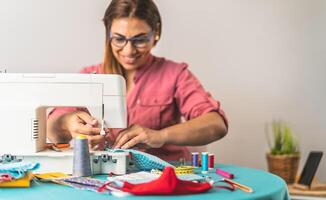 Happy Latin tailor seamstress woman sewing with machine homemade medical face mask for preventing and stop corona virus spreading - textile industry and covid19 healthcare concept photo