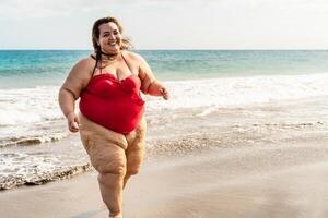 Happy plus size woman running on the beach - Curvy overweight model having fun during vacation in tropical destination - Over size confident person concept photo