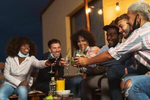 Happy multiracial friends having fun during holidays toasting with cocktails and red wine on patio house party photo