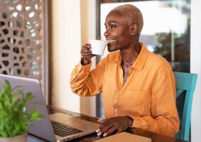 African senior woman drinking coffee while using laptop in bar restaurant - Smart working concept photo