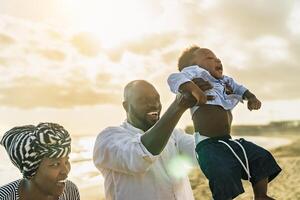 Happy African family having fun on the beach during summer holidays - Parents love concept photo