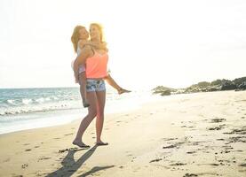 Happy loving family of mother and daughter having fun and playing on the beach - Young red hair mom carrying her  kid on piggyback and walking near the sea - Family, motherhood, childhood concept photo