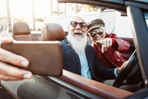 contento mayor Pareja tomando selfie en nuevo convertible coche - maduro personas teniendo divertido en cabriolé juntos durante la carretera viaje vacaciones - mayor estilo de vida y viaje transporte concepto foto