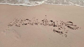 Gentle waves washing over the word Holidays written in sand on a beach, symbolizing summer vacations and relaxation video