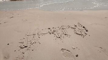 Handwritten Happy message on sandy beach with gentle waves, capturing the concept of joy and relaxation, potentially related to summer or vacation themes video