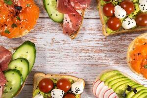 An assortment of sandwiches with fish, cheese, meat and vegetables lay on the wooden table photo
