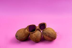 three whole coconuts and wooden glasses on a pink background photo