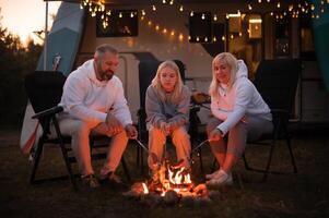 A family cooks sausages on a bonfire near their motorhome in the woods photo