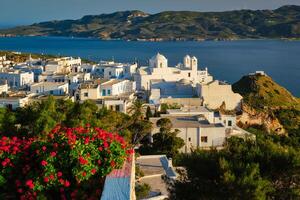 Picturesque scenic view of Greek town Plaka on Milos island over red geranium flowers photo