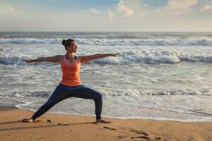 Woman doing yoga asana Virabhadrasana 1 Warrior Pose on beach on photo