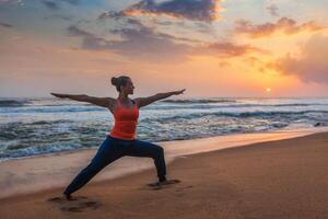 Woman doing yoga asana Virabhadrasana 1 Warrior Pose on beach on photo