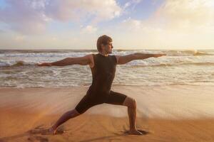 Man doing yoga asana Virabhadrasana 1 Warrior Pose on beach photo