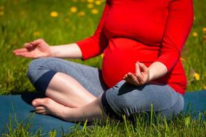 Pregnant woman doing asana Sukhasana outdoors photo