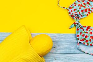 Top view of a swimsuit and a melon in a bag, lying on a blue wooden and yellow background.Summer vacation concept photo