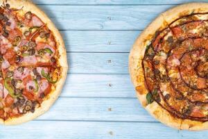 Two different delicious big pizzas on a blue wooden background photo