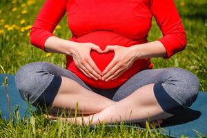 Pregnant woman doing asana Sukhasana outdoors photo