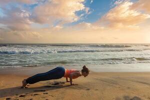 Woman practices yoga at the beach on sunset photo