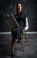 a young brunette female artist stands behind an easel. photo