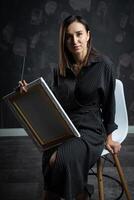 a young brunette female artist stands behind an easel. photo