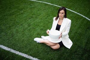 A business woman with a large cup, sitting on a green lawn in the park. photo