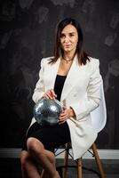 Portrait of a woman holding a silver disco ball. Taken in a photo studio.