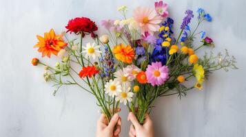 ai generado un par de manos suavemente sostiene un vibrante ramo de flores de clasificado flores en contra un texturizado gris fondo. naturaleza vistoso paleta. foto