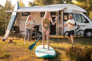 the family is resting next to their mobile home. My daughter is standing with a paddle on a sup board, and her parents pour water on her photo