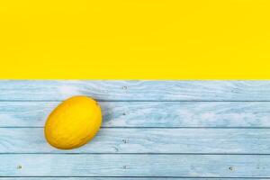 A whole yellow melon lies on a blue wooden background and a yellow background photo
