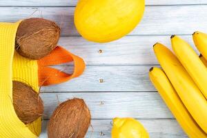 Whole coconuts in a yellow bag, bananas and melon on a blue wooden background photo