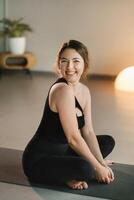 A girl in black sportswear is sitting on a yoga mat and smiling photo